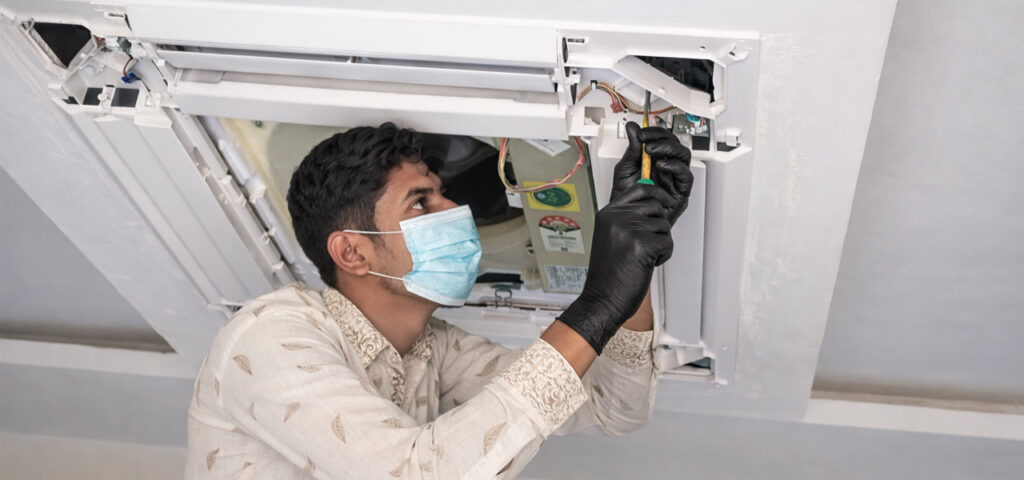 Technician servicing ceiling cassette AC indoor unit
